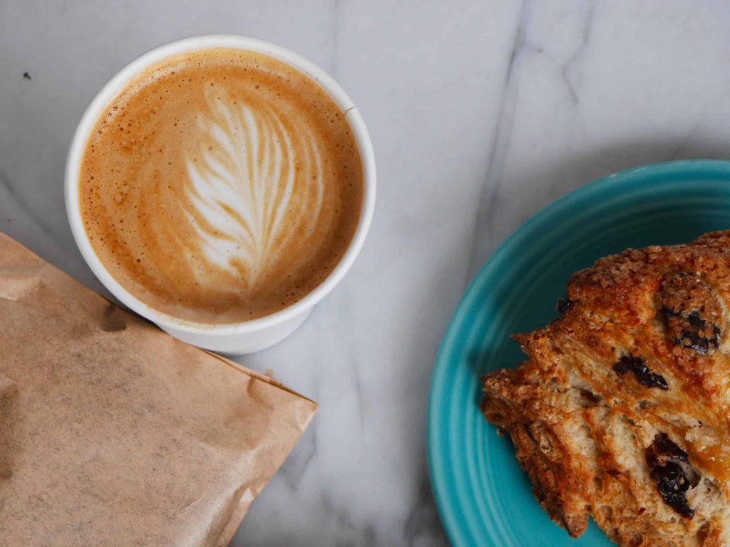 Coffee with latte art and a chocolate chip muffin on a blue plate.